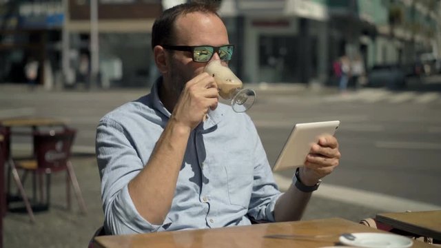 Young man using tablet computer and drinking coffee in cafe in city
