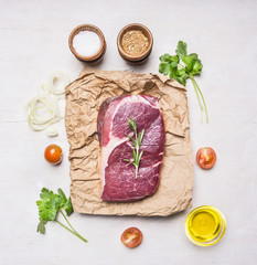 appetizing beef steak on a paper packaging with herbs, cherry tomatoes, seasonings and butter, top view, on a rustic wooden background