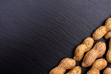 Unclean peanuts lie on a black stone board in the form of a frame, space for text