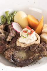 Baked beef marrow with vegetables, decorated with purple leafs, placed on white plate, light background, isolated