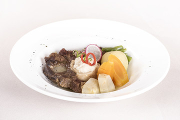 Baked beef marrow with vegetables, decorated with purple leafs, placed on white plate, light background, isolated