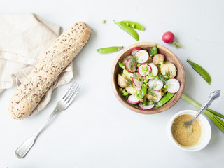 A wooden bowl of spring vegetable salad with mustard dressing on grey background.