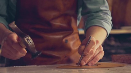 The master makes shoes in the workshop. Press leather with hammer to make holes 