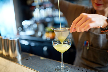bartender pouring cocktail into glass at bar