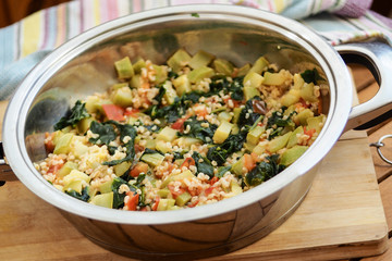 Delicious homemade vegetarian bulgur (couscous) with vegetables:spinach, carrots, zucchini, tomatoes and dill in pan.