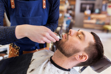 Obraz na płótnie Canvas man and barber with trimmer cutting beard at salon