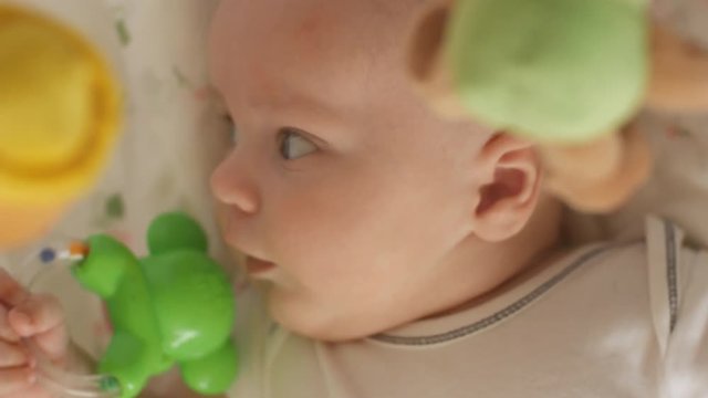 Top view shot of cute baby with soother lying in crib and looking at spinning taddy bear toys. The baby looks around and then smiles and laughs. Concept of caring for children, parental love and lack