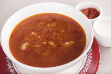 Tomato soup, served with sour cream and extra tomato sauce, white and red plate, light background, isolated