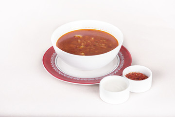 Tomato soup, served with sour cream and extra tomato sauce, white and red plate, light background, isolated
