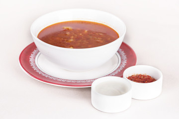 Tomato soup, served with sour cream and extra tomato sauce, white and red plate, light background, isolated