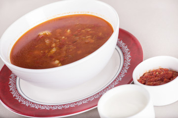 Tomato soup, served with sour cream and extra tomato sauce, white and red plate, light background, isolated