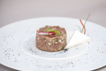 Classic beef tartar, served with slices of cheese and decorated with herbs, isolated on light background, white plate