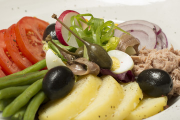 Tuna salad with vegetables, placed on a white plate, brown background