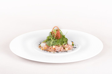 Fresh smoked salmon salad, served with rucola and baby spinach and pieces of vegetables, decorated with herbs, placed on white plate, light background, isolated