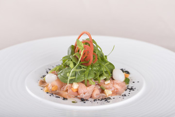 Fresh smoked salmon salad, served with rucola and baby spinach and pieces of vegetables, decorated with herbs, placed on white plate, light background, isolated