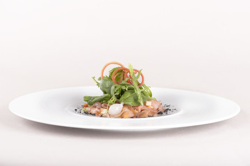Fresh smoked salmon salad, served with rucola and baby spinach and pieces of vegetables, decorated with herbs, placed on white plate, light background, isolated