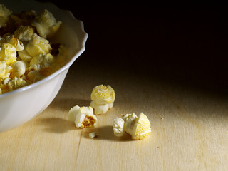 popcorn in a bowl on a wooden table in darkness partial illuminated, copy space