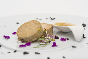Liver terrine served with sweet sauce, decorated with flower petals, green leafs and black salt, placed on white plate, light background, isolated