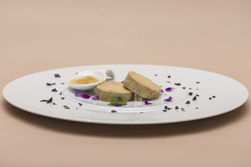 Liver terrine served with sweet sauce, decorated with flower petals, green leafs and black salt, placed on white plate, light background, isolated
