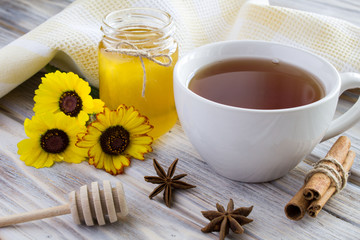 Tea, honey, cinnamon and flowers on the light brown wooden background 