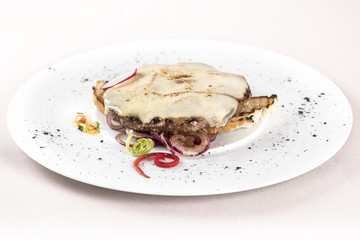 Pork steak with cheese, placed on toast and red onion, decorated with green and red leafs, placed on white plate, light background, isolated