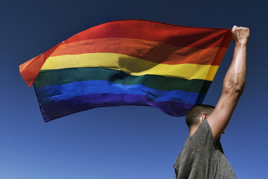 Side view of man holding rainbow flag against blue sky
