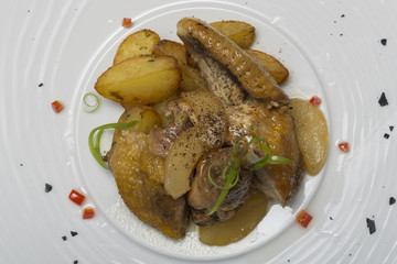 Roasted guinea fowl with potatoes, with green herbs, placed on a white plate, brown background