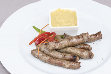 Homemade sausages, served with mustard and decorated with herbs, isolated on light background, white plate