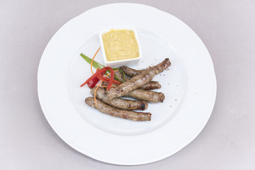 Homemade sausages, served with mustard and decorated with herbs, isolated on light background, white plate