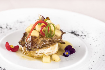 Luxurious dish with duck liver, pineapple and mango pieces, sweet sauce, placed on toasted bread, decorated with eatable flowers and red and green leafs, placed on white plate, light background, isola