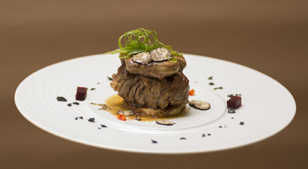 Sliced truffles topped on a grilled steak, beef and pork, with vegetable and sauce, on a white plate, brown background