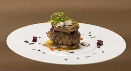 Sliced truffles topped on a grilled steak, beef and pork, with vegetable and sauce, on a white plate, brown background