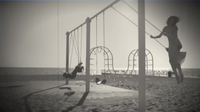 Young beautiful brunette woman is riding on a swing and smiling in retro style.