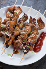 Close-up of wooden skewers with grilled chicken breast served on a white glass plate
