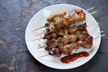 White glass plate with bbq chicken fillet skewers, brown stone background, studio shot