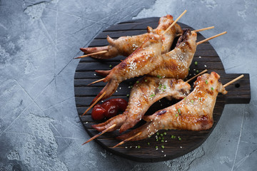 Black wooden serving board with roasted chicken wings on skewers. High angle view on a grey stone background with copyspace