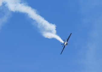 Pilot doing beautiful maneuvers with a propeller plane on a sunny day. White smoke as trail. Blue sky in the background. 