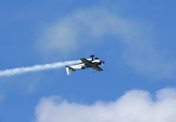 Pilot doing beautiful maneuvers with a propeller plane on a sunny day. White smoke as trail. Blue sky in the background. 
