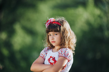Cute little model girl in white dress on nature background. Crossed arms.