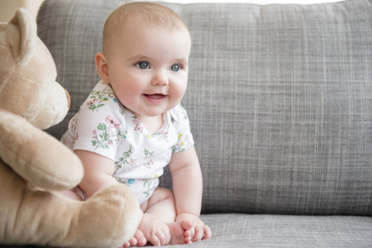 Baby girl with teddy bear sitting on sofa