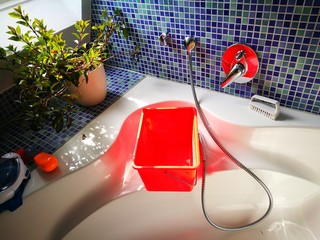 Rechteckiger Putzeimer in leuchtendem Orange auf dem Rand der Badewanne in einem Badezimmer in...