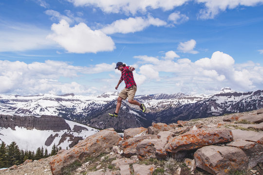 Mid adult man jumping over rocks in mountains