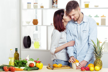 happy couple in love in kitchen making healthy juice from fresh orange. couple is kissing