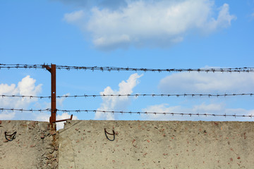 Concrete fence with barbed wire on a background of blue sky.