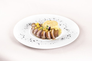 Luxurious dish with slices of duck breast, pineapple pieces, sweet sauce, with potato puree and parmesan, decorated with eatable flowers and red and green leafs, placed on white plate, light backgroun