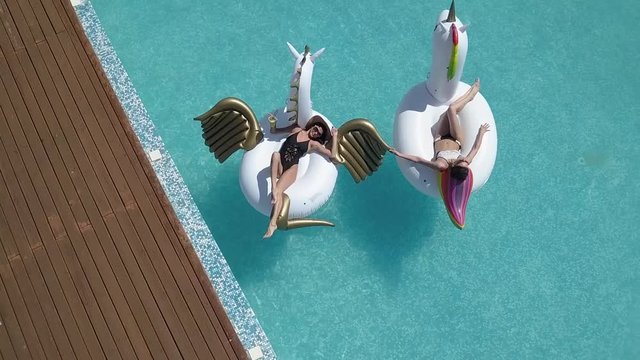 Aerial - young women sunbathing on air mattresses the unicorn and the Pegasus. Attractive young girls rest on a sunny day in pool. Shooting with quadrocopter