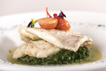Perch fillet with spinach, sauce and tomato, decorated with eatable flowers and red leafs, placed on white plate, light background, isolated