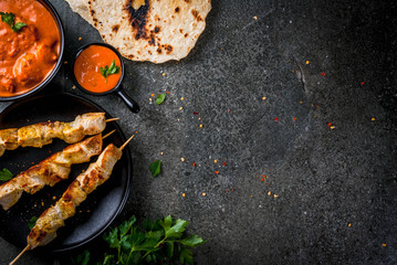 Indian food. Traditional dish spicy chicken tikka masala, butter chicken curry, with indian naan butter bread, spices, herbs. Served in bowl. sauce, on skewers. Stone dark table. copy space top view