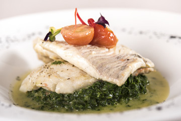 Perch fillet with spinach, sauce and tomato, decorated with eatable flowers and red leafs, placed on white plate, light background, isolated