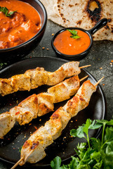 Indian food. Traditional dish spicy chicken tikka masala, butter chicken curry, with indian naan butter bread, spices, herbs. Served in bowl. sauce, on skewers. Stone dark table. copy space